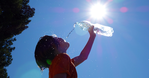Jongen staat buiten in de zon en gooit uit een fles water op zijn hoofd.